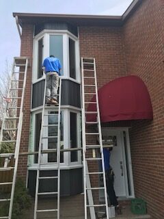A man on a ladder painting the outside of a building.