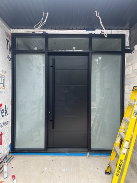 A black door with frosted glass panels in front of a yellow ladder.